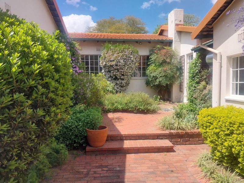 A charming rear courtyard featuring brick paving, tiered steps, and established garden landscaping, framed by the property's exterior walls and terracotta roof.