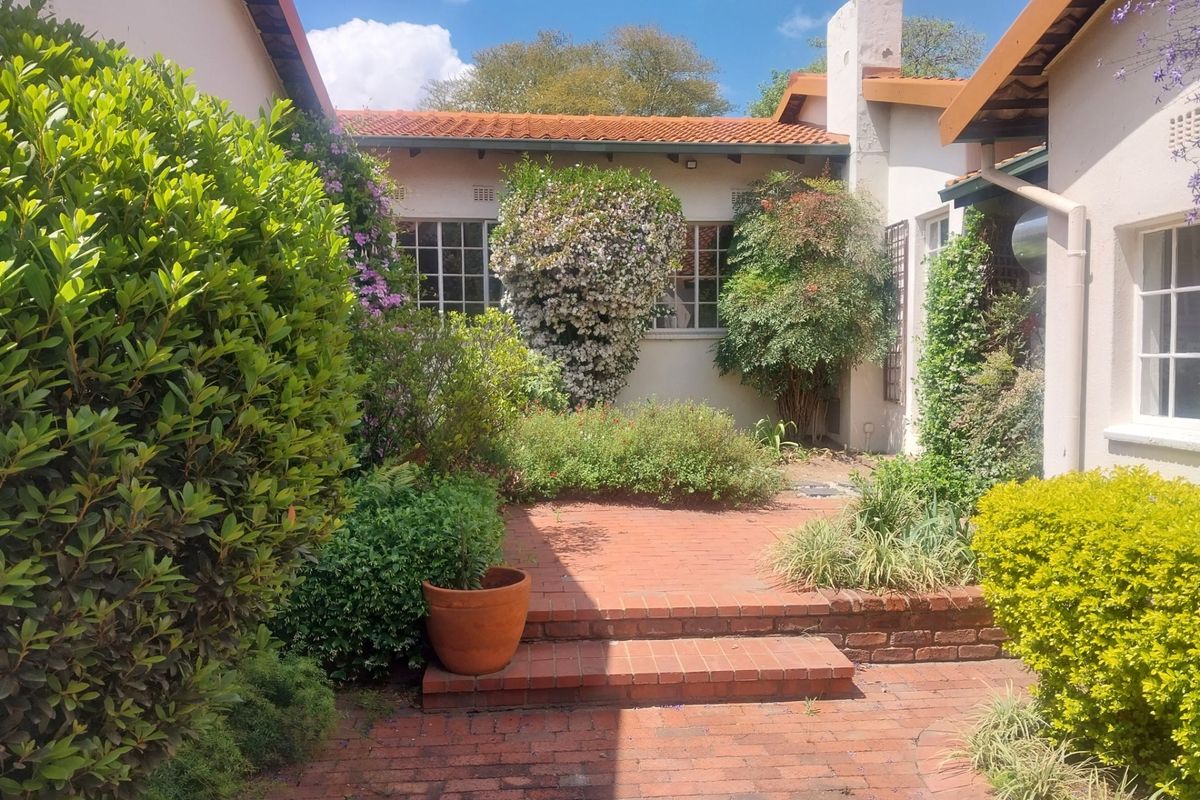 A charming rear courtyard featuring brick paving, tiered steps, and established garden landscaping, framed by the property's exterior walls and terracotta roof.