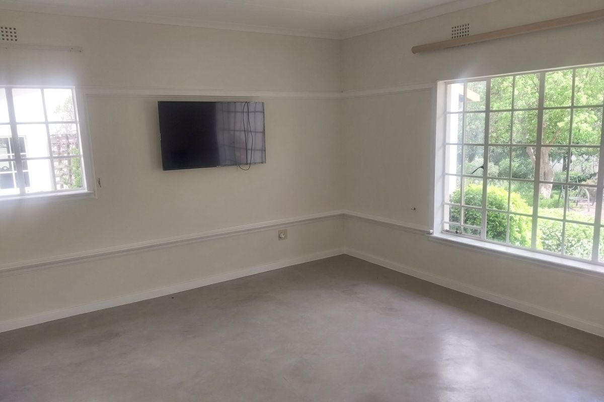 A bright, empty living room featuring polished concrete floors, large windows with garden views, and classic chair rail molding.