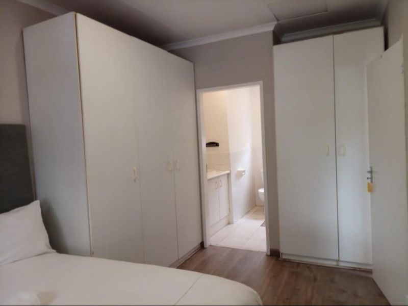 Bedroom featuring laminate flooring and ample built-in cupboard storage, with direct access to an en-suite bathroom.