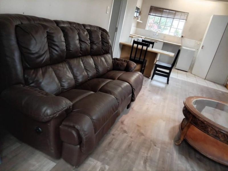 Open-plan living area featuring laminate flooring and an adjacent kitchen with built-in cabinetry and sink.