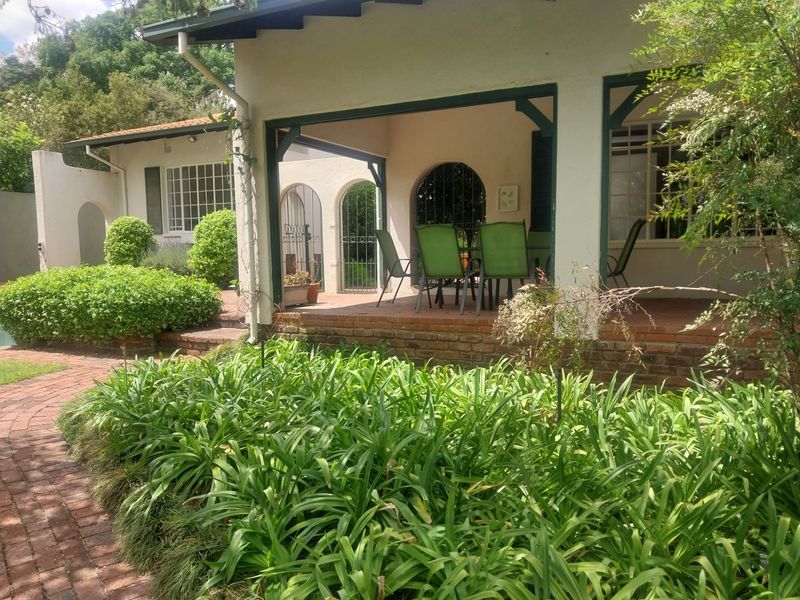A covered brick-paved patio featuring arched architectural details and wrought iron security gates, overlooking a lush garden with a brick pathway.