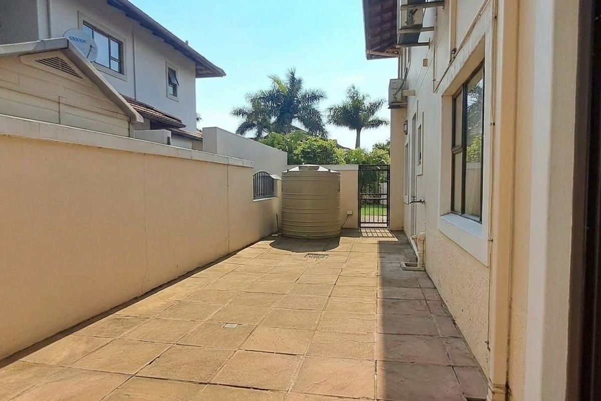 A paved rear courtyard area featuring a boundary wall, water storage tank, and access gate, providing a functional outdoor utility space.