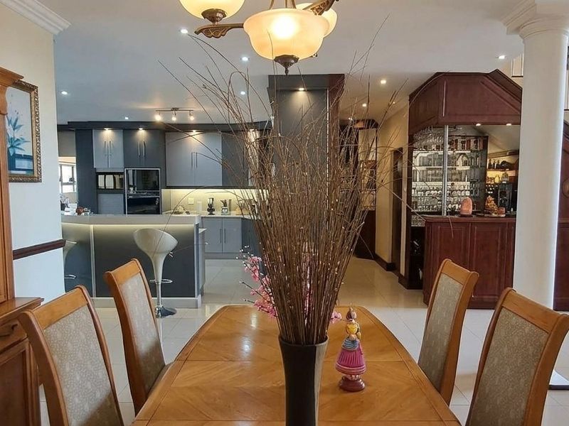 Spacious open-plan living area featuring a modern kitchen with island, a built-in bar, and a grand staircase, finished with high-quality tiling throughout.
