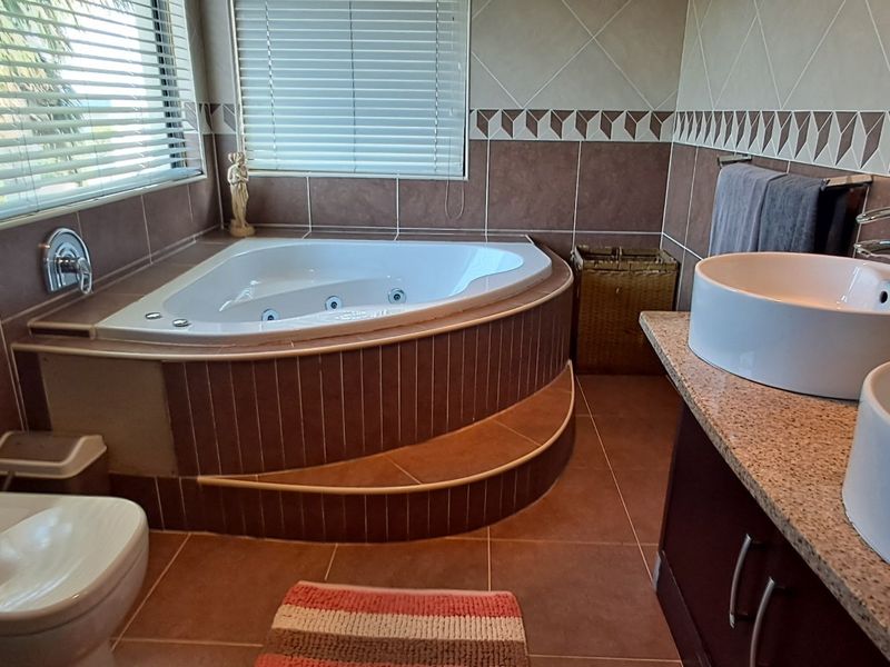 A spacious bathroom featuring a corner spa bath, double vanity with vessel sinks, granite countertops, and neutral tiled finishes throughout.
