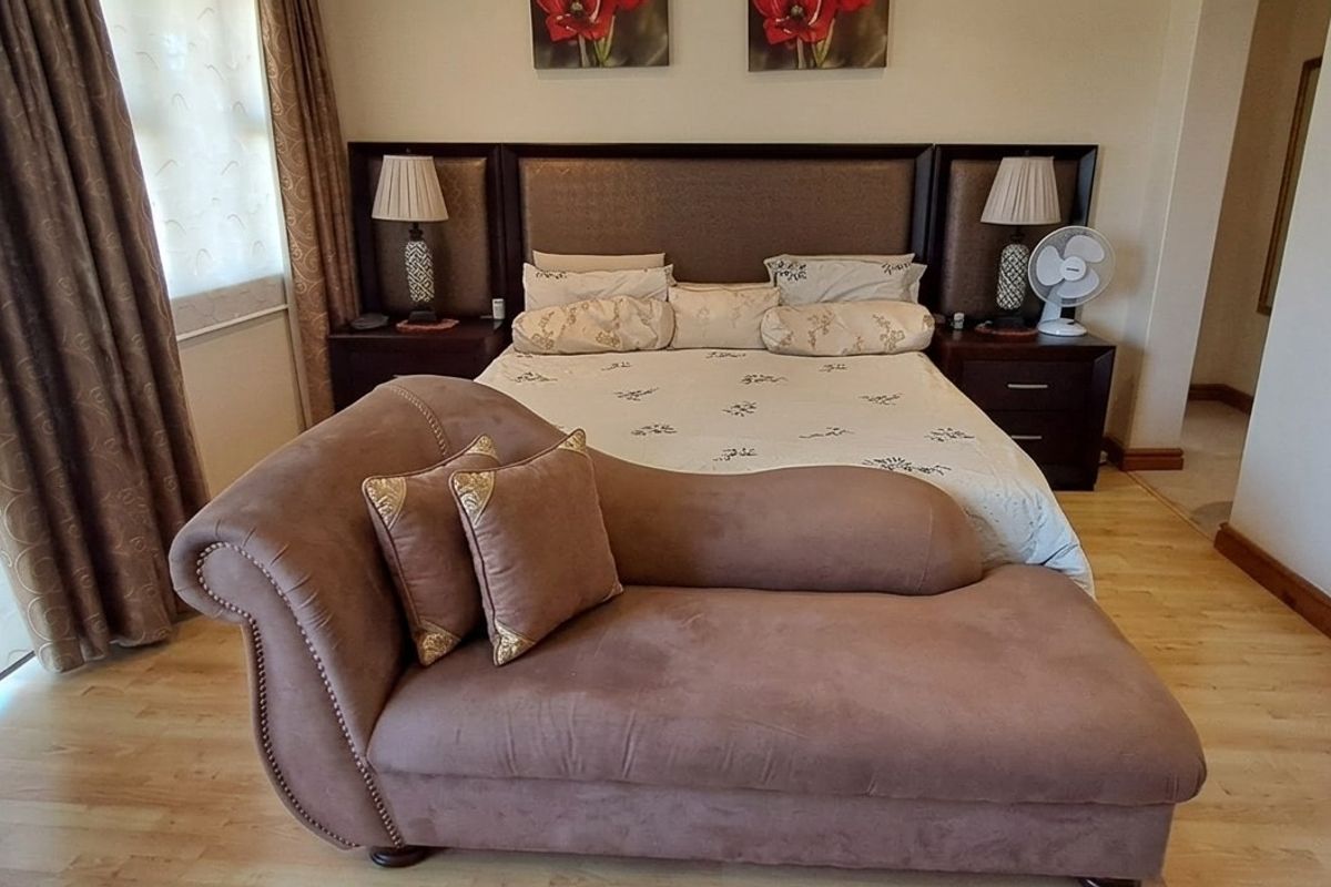 A well-maintained bedroom featuring light-toned laminate flooring, neutral walls, and a built-in headboard with integrated bedside tables.