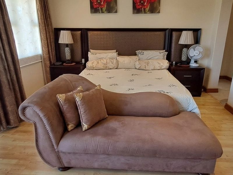 A well-maintained bedroom featuring light-toned laminate flooring, neutral walls, and a built-in headboard with integrated bedside tables.
