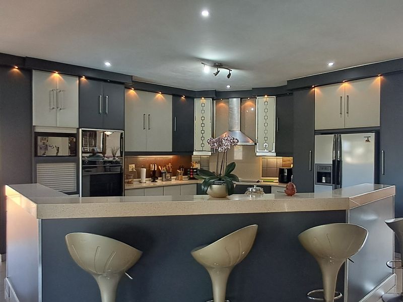 Modern kitchen featuring two-tone cabinetry, stone countertops, a breakfast bar, and integrated stainless steel appliances with recessed lighting.