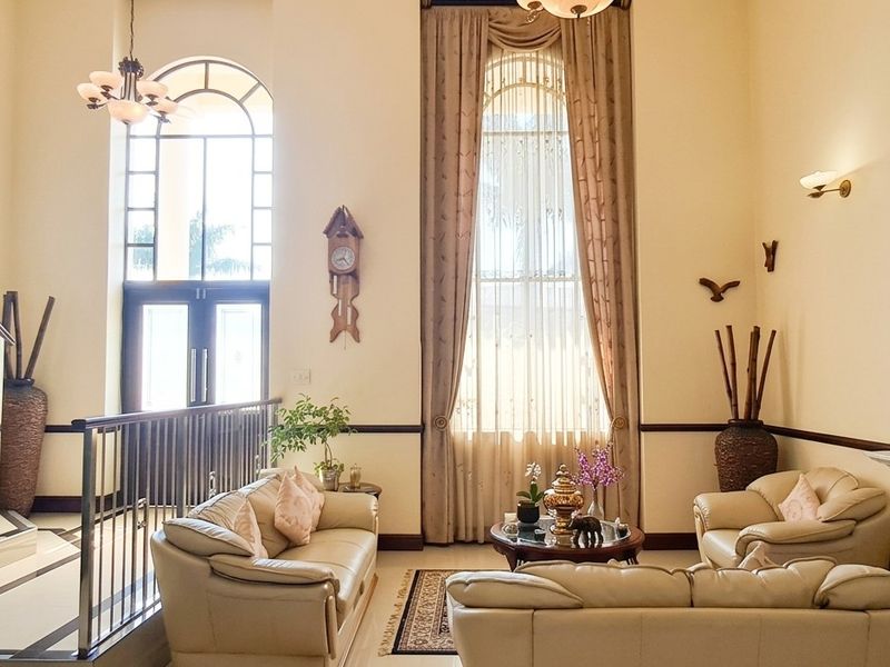 Spacious double-volume living room featuring a grand staircase, elegant arched windows, and a classic fireplace, creating an airy and sophisticated atmosphere.