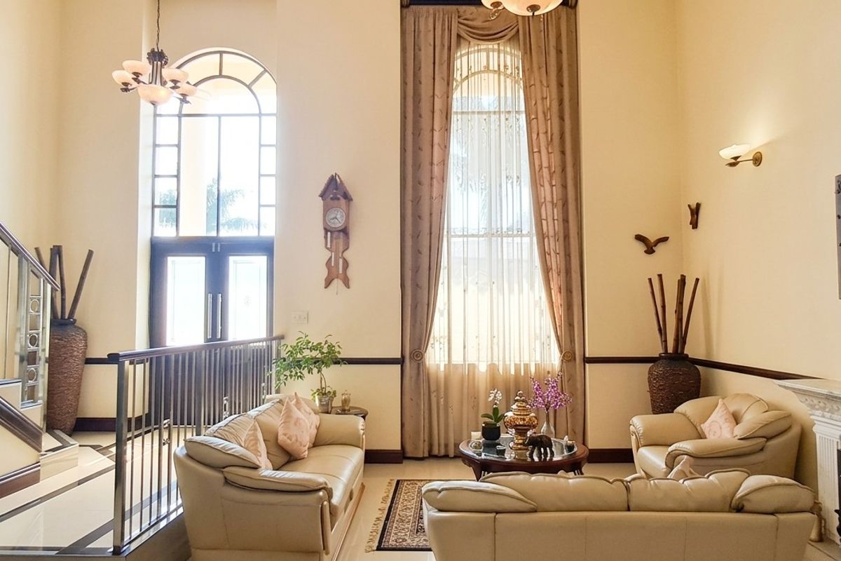 Spacious double-volume living room featuring a grand staircase, elegant arched windows, and a classic fireplace, creating an airy and sophisticated atmosphere.