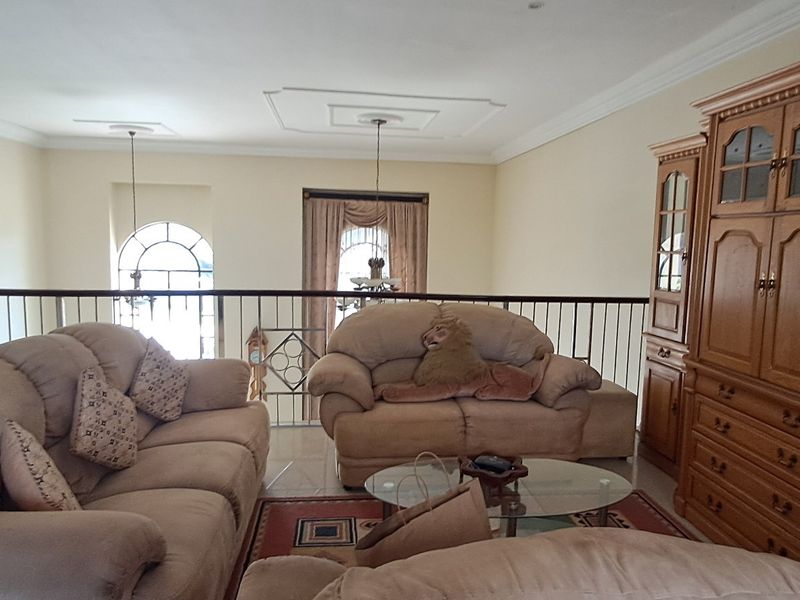Spacious living area featuring tiled flooring, decorative ceiling roses, and a metal balustrade overlooking the lower level.