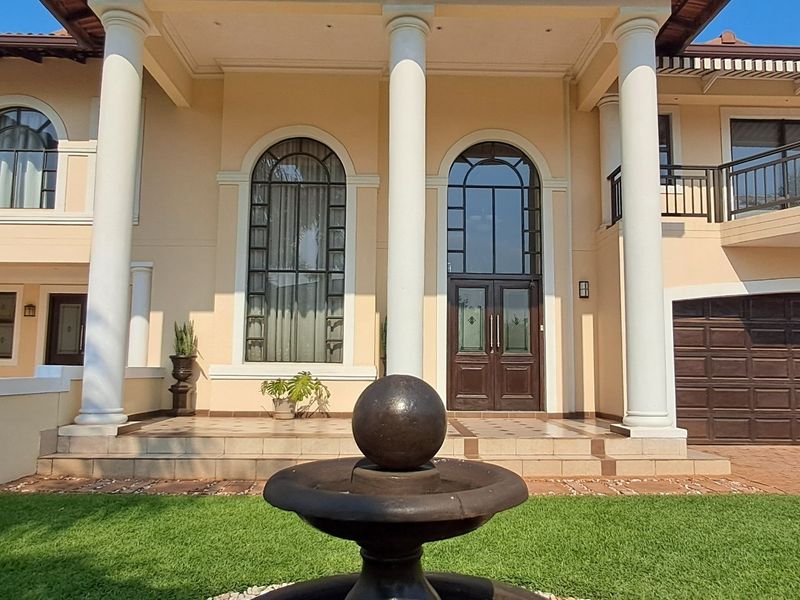 Impressive double-storey residence featuring a grand entrance with classical columns, arched windows, a tiled porch, and a spacious double garage.