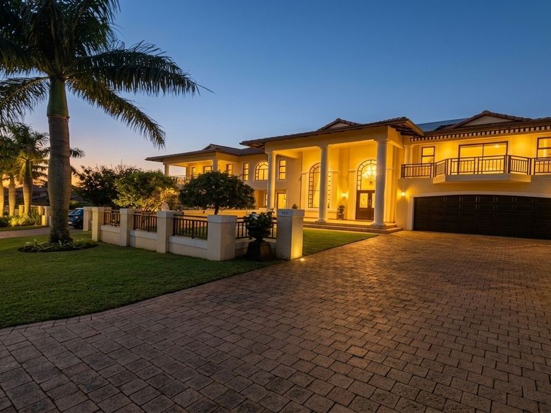 A stunning double-story luxury residence at dusk, featuring a paved driveway, double garage, elegant columns, and a well-maintained landscaped garden with exterior lighting.