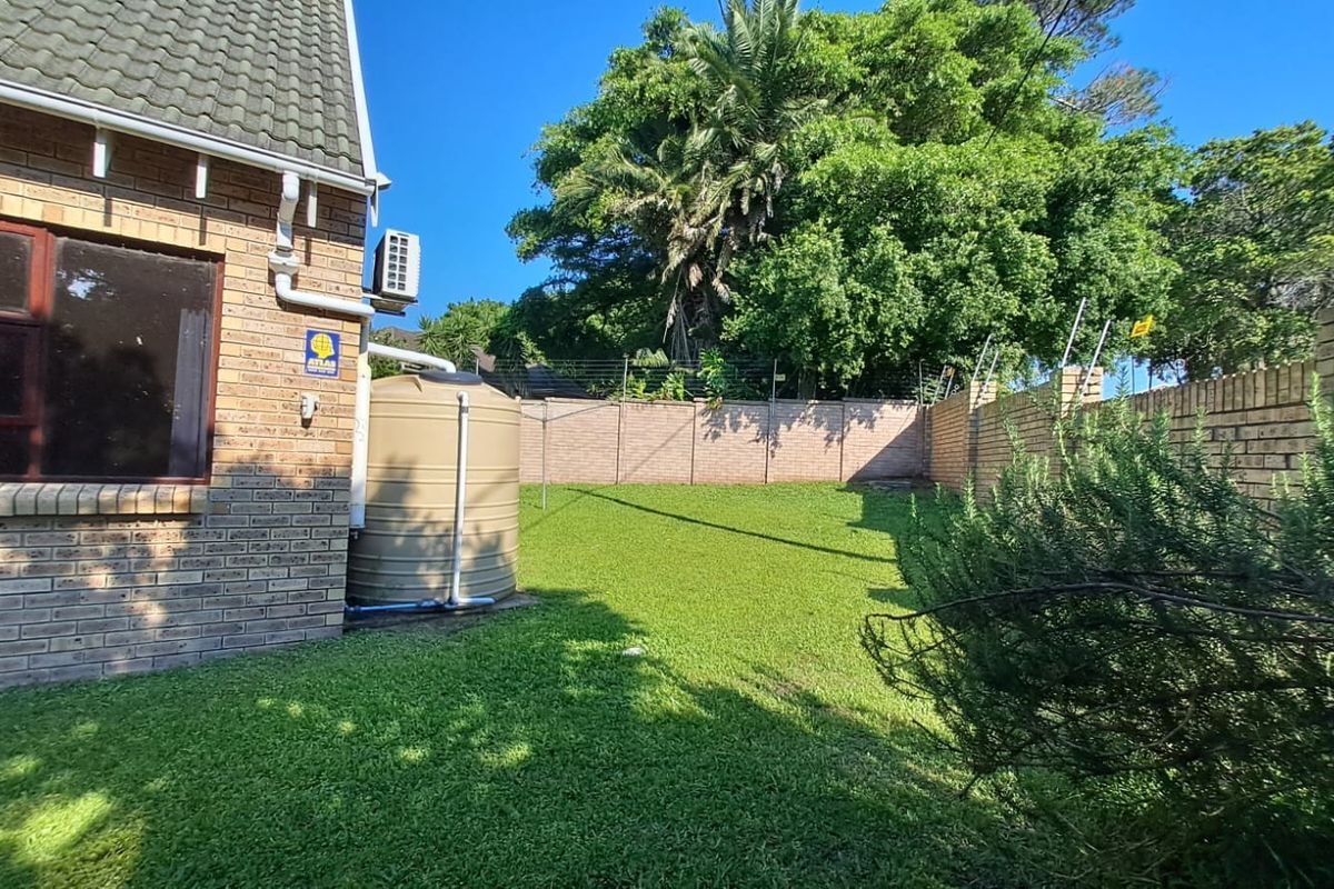 A private rear garden featuring a well-maintained lawn, face brick boundary walls with electric fencing, and a dedicated water storage tank.