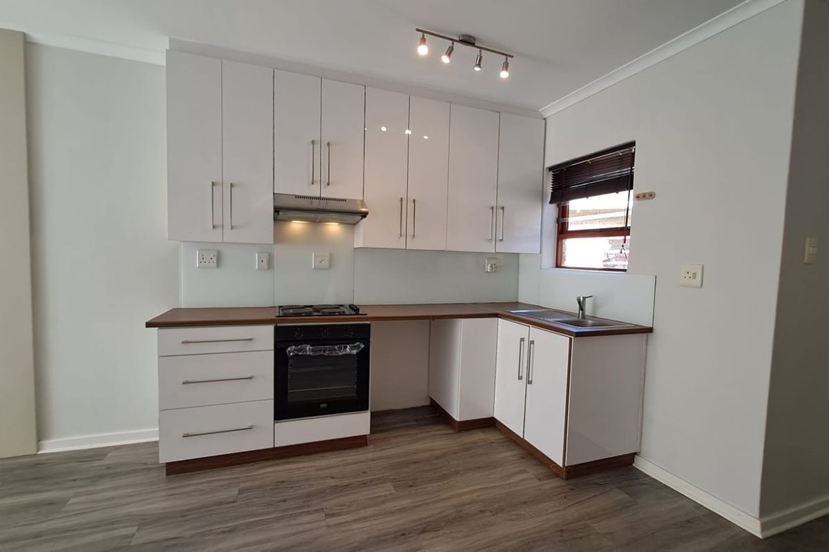 Modern kitchen featuring white cabinetry, laminate countertops, built-in oven, gas hob, and extractor fan, finished with durable laminate flooring.