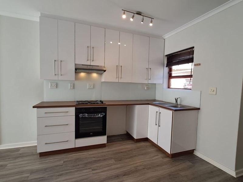 Modern kitchen featuring white cabinetry, laminate countertops, built-in oven, gas hob, and extractor fan, finished with durable laminate flooring.