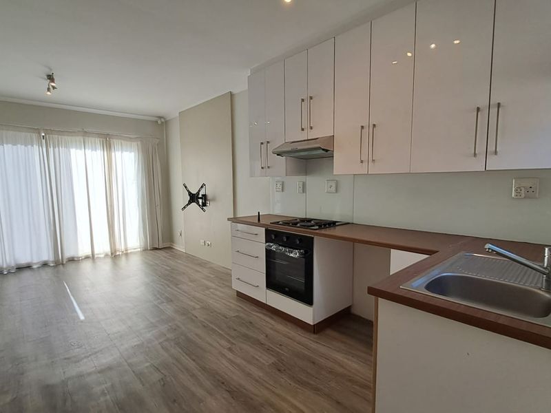 Modern open-plan living area featuring a sleek kitchen with white cabinetry, built-in appliances, and direct access to a bright living space with sliding doors.