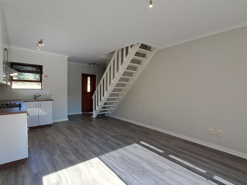 Open-plan living area featuring modern laminate flooring, a compact kitchen with built-in cabinetry, and a staircase leading to the upper level.