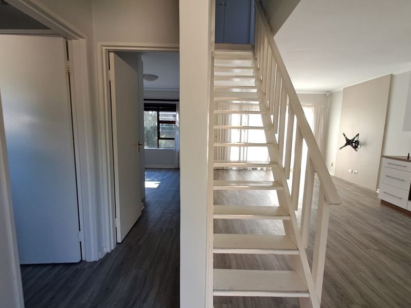 Open plan living area featuring a central staircase, modern laminate flooring, and a functional kitchen with built-in cabinetry and appliances.
