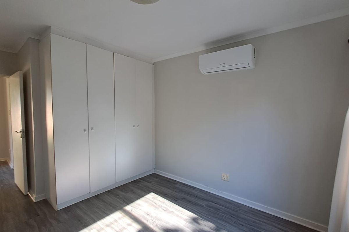 A bright, neutral bedroom featuring modern laminate flooring, ample built-in cupboard storage, and a wall-mounted split-system air conditioning unit.