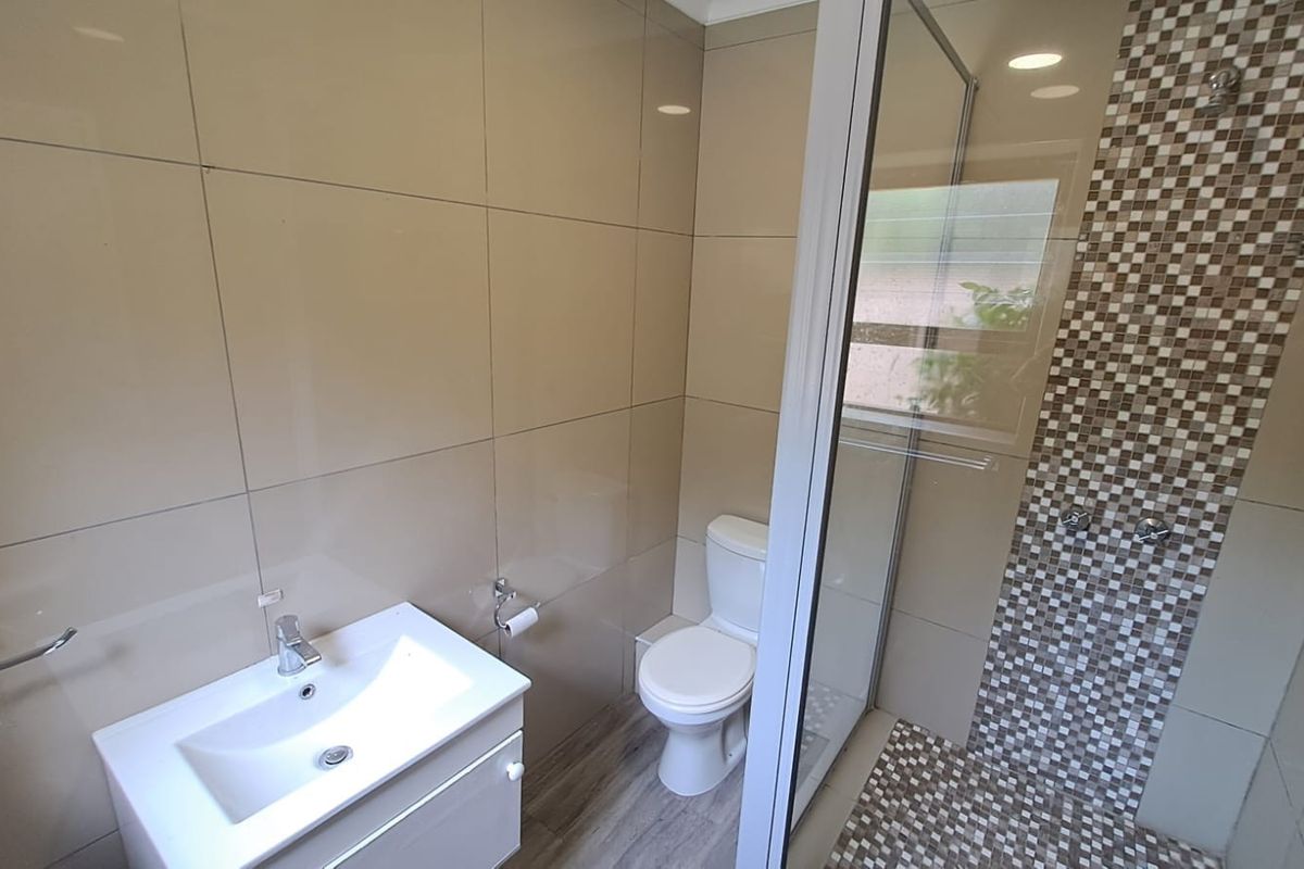 Modern bathroom featuring a vanity basin, toilet, and a glass-enclosed shower with a decorative mosaic tile accent wall.