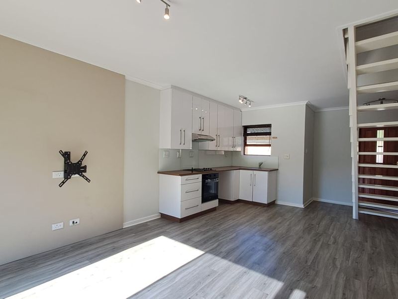 Open-plan living area featuring a modern kitchen with built-in cabinetry, integrated appliances, and a staircase leading to the upper level.