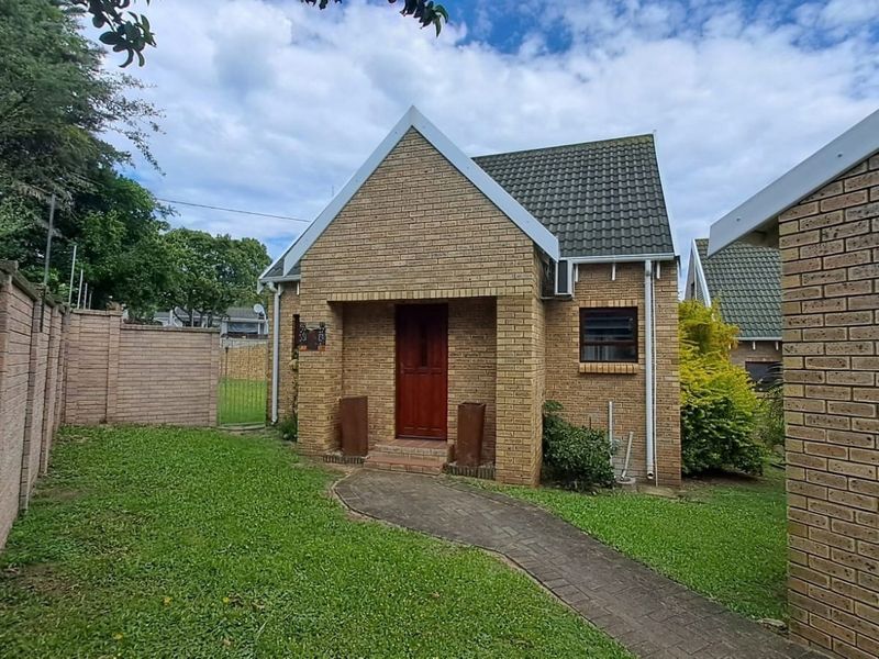 Front view of a face brick townhouse featuring a tiled roof, paved walkway, and a private garden area with boundary walling.