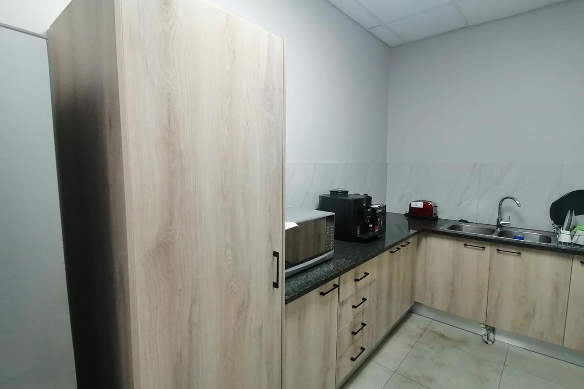 A functional industrial kitchen area featuring light wood-grain cabinetry, granite countertops, a double stainless steel sink, and tiled flooring.