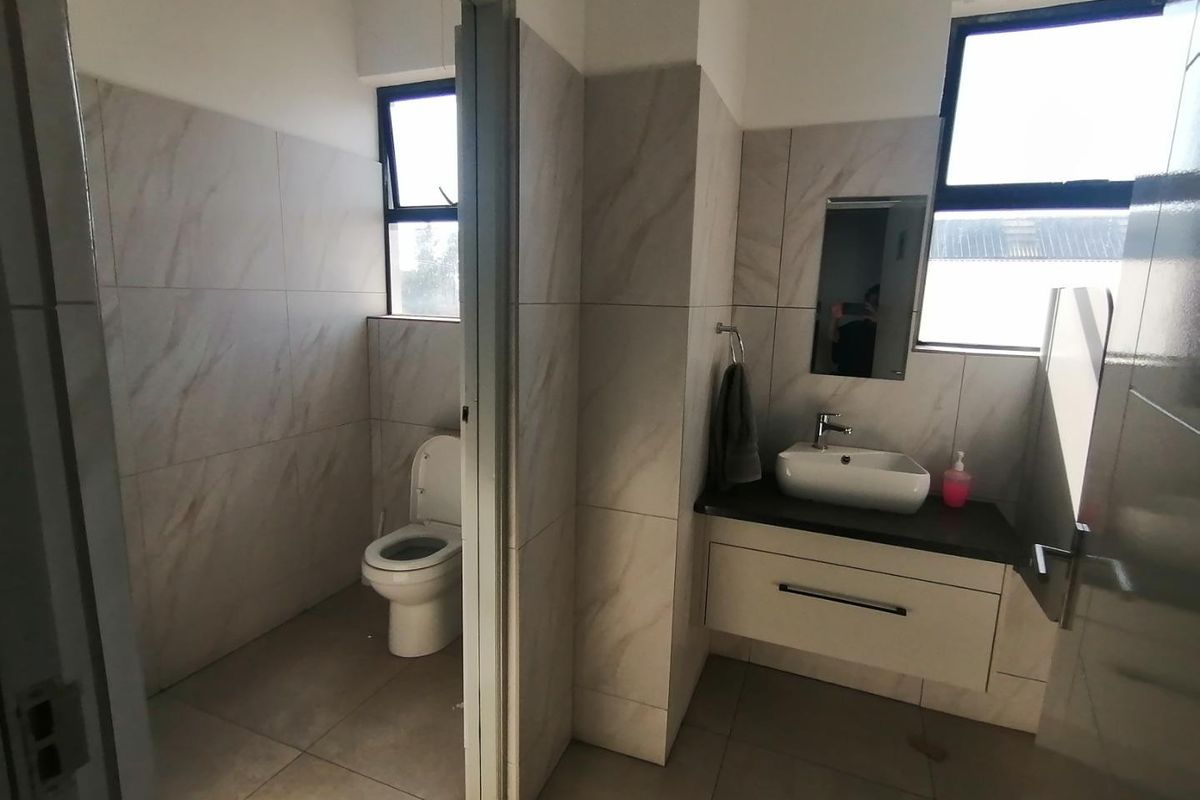 A clean, modern bathroom featuring tiled walls and flooring, a wall-mounted vanity with a vessel sink, and a separate toilet area.