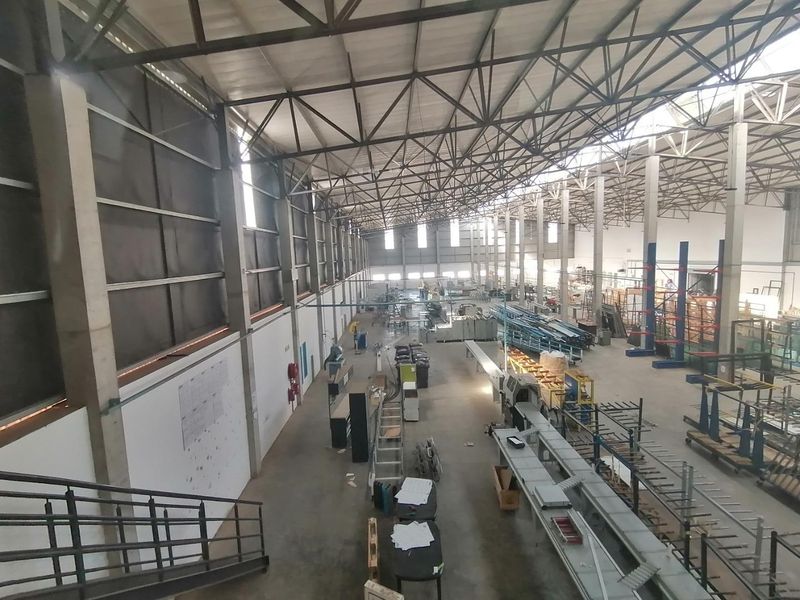 Spacious industrial warehouse featuring high ceilings with exposed steel trusses, concrete flooring, and large-scale manufacturing infrastructure.