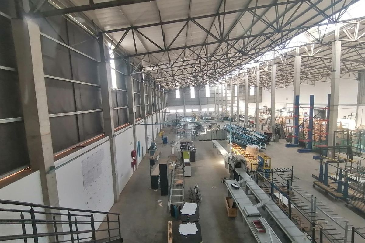 Spacious industrial warehouse featuring high ceilings with exposed steel trusses, concrete flooring, and large-scale manufacturing infrastructure.