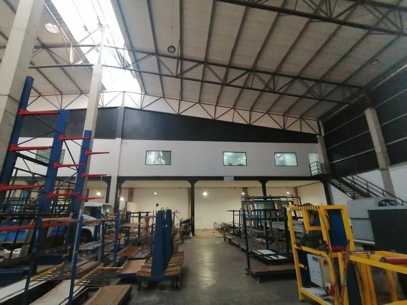 Spacious industrial warehouse featuring a high-clearance steel truss roof, mezzanine level with staircase, and durable concrete flooring suitable for manufacturing or storage operations.