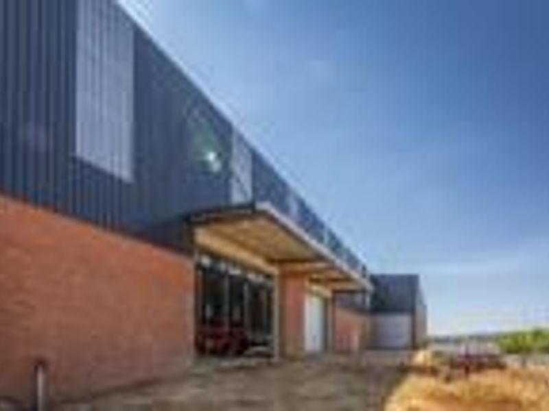 Modern industrial building exterior featuring a combination of brick and corrugated metal cladding with a covered entrance canopy and large glass storefront.