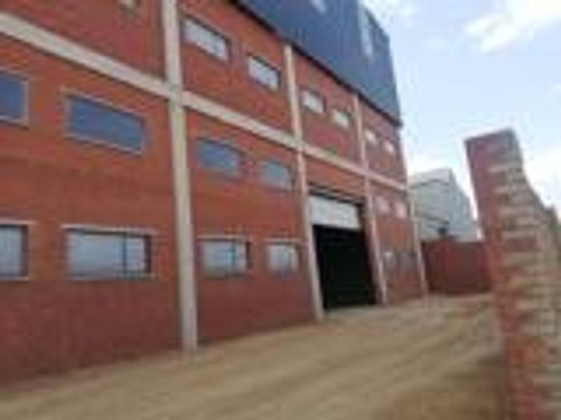 A multi-story industrial building featuring a red brick facade, concrete structural columns, and a large roller shutter door entrance.