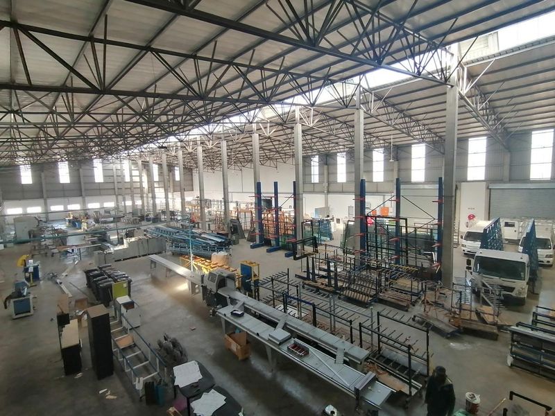 Spacious industrial warehouse featuring high-clearance steel truss roofing, concrete flooring, and large roller shutter access points suitable for manufacturing or logistics operations.