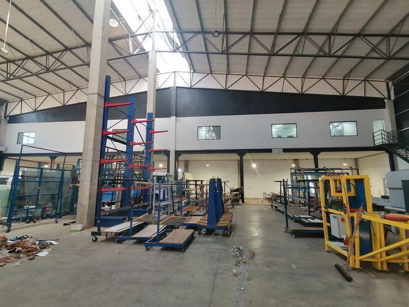 Spacious industrial warehouse featuring high steel truss ceilings, concrete flooring, and a mezzanine level, suitable for manufacturing or storage operations.