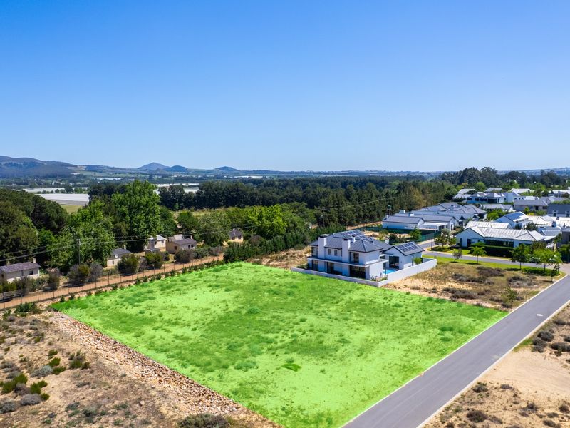 An aerial view of a vacant residential plot situated in a developed estate, featuring clear boundaries and access to a paved road.