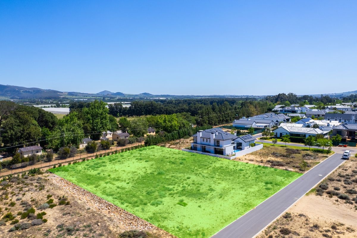 An aerial view of a vacant residential plot situated in a developed estate, featuring clear boundaries and access to a paved road.
