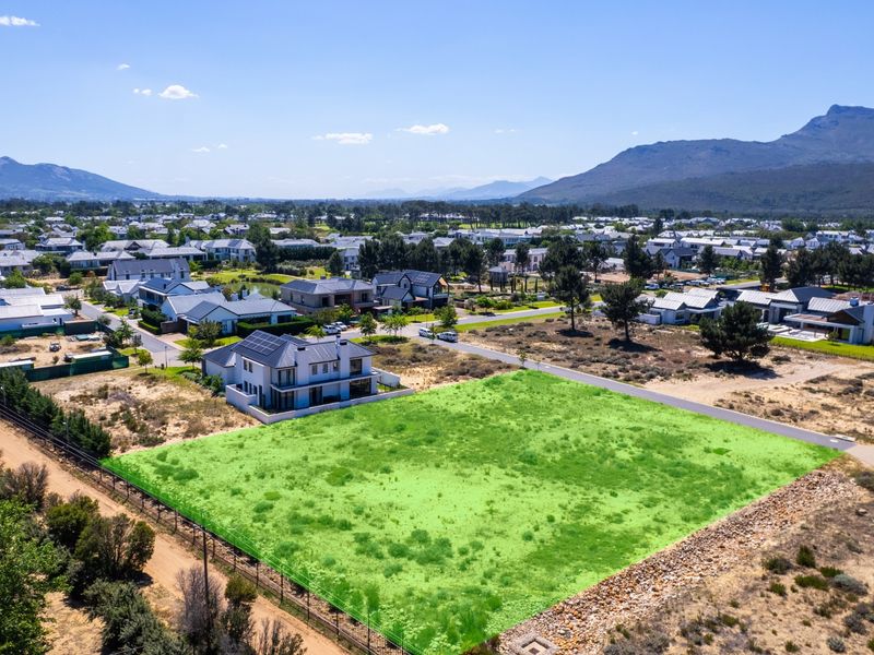 Aerial view of a vacant residential plot in a developed estate, featuring clear boundaries and surrounding mountain views.