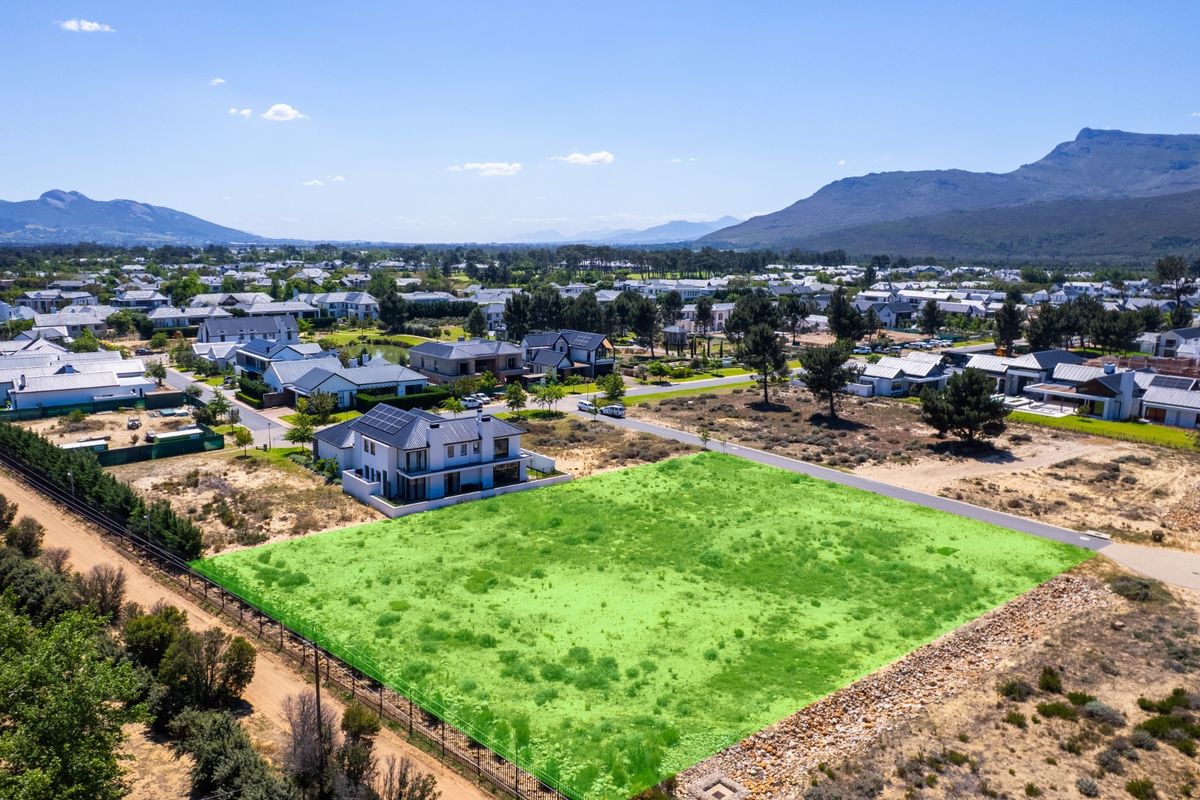 Aerial view of a vacant residential plot in a developed estate, featuring clear boundaries and surrounding mountain views.