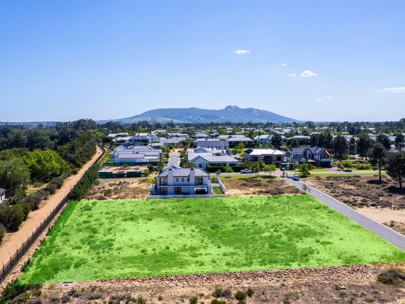 An aerial view of a vacant residential plot situated in a developed estate, featuring road access and scenic mountain views.