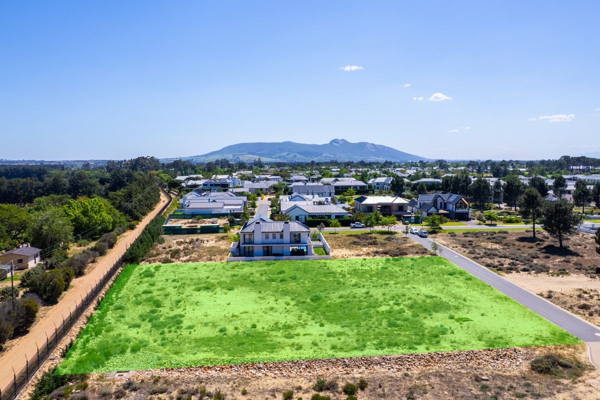 An aerial view of a vacant residential plot situated in a developed estate, featuring road access and scenic mountain views.