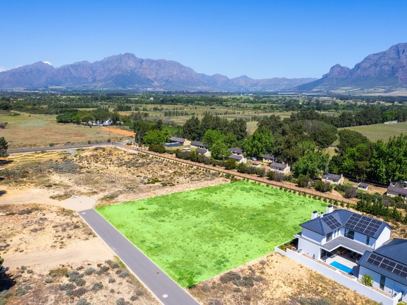 Aerial view of a vacant residential plot with mountain views, adjacent to an existing modern home with solar panels.