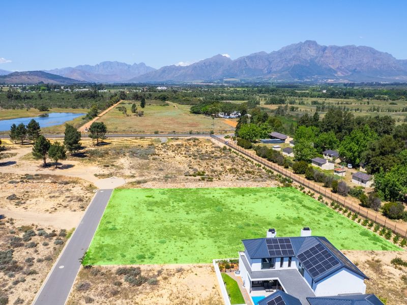 Aerial view of a residential vacant land plot with mountain views, featuring adjacent paved road access and nearby established residential infrastructure.