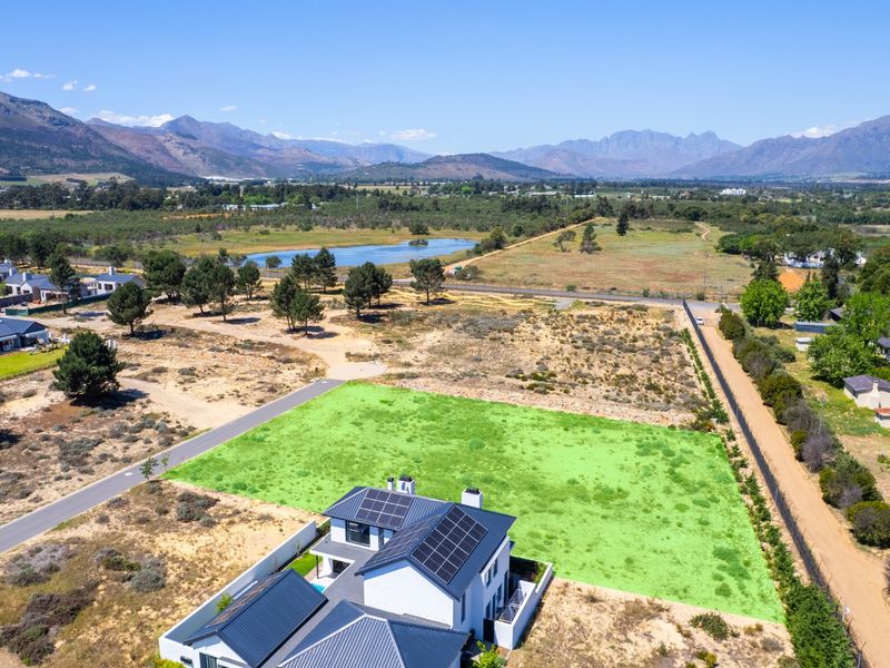 Aerial view of a residential property featuring a modern home with solar panels, situated on a large plot with surrounding landscape and mountain views.