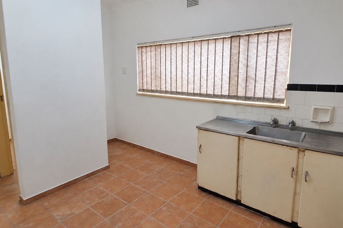 A functional, empty kitchen space featuring tiled flooring, a stainless steel sink, and built-in cabinetry with a tiled backsplash.