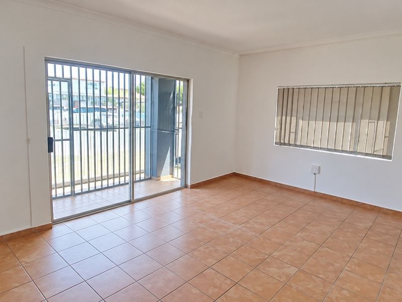 A bright, empty office space featuring tiled flooring, a sliding glass door with security gate, and vertical blinds for adjustable natural light.