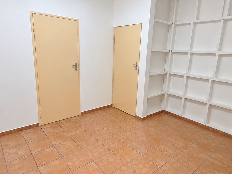 An empty office space featuring tiled flooring, two interior doors, and extensive built-in wall shelving.