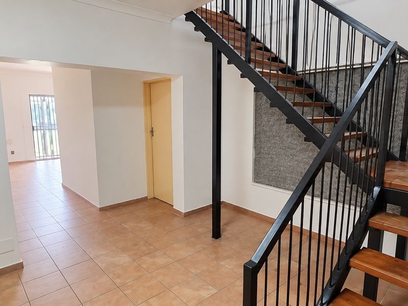 An open-plan entrance area featuring a modern staircase with wooden treads and a black metal balustrade, complemented by neutral tiled flooring.