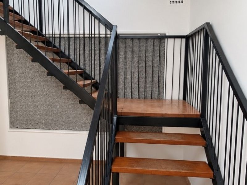 A bright hallway featuring a modern metal staircase with wooden treads, tiled flooring, and a skylight providing natural overhead lighting.